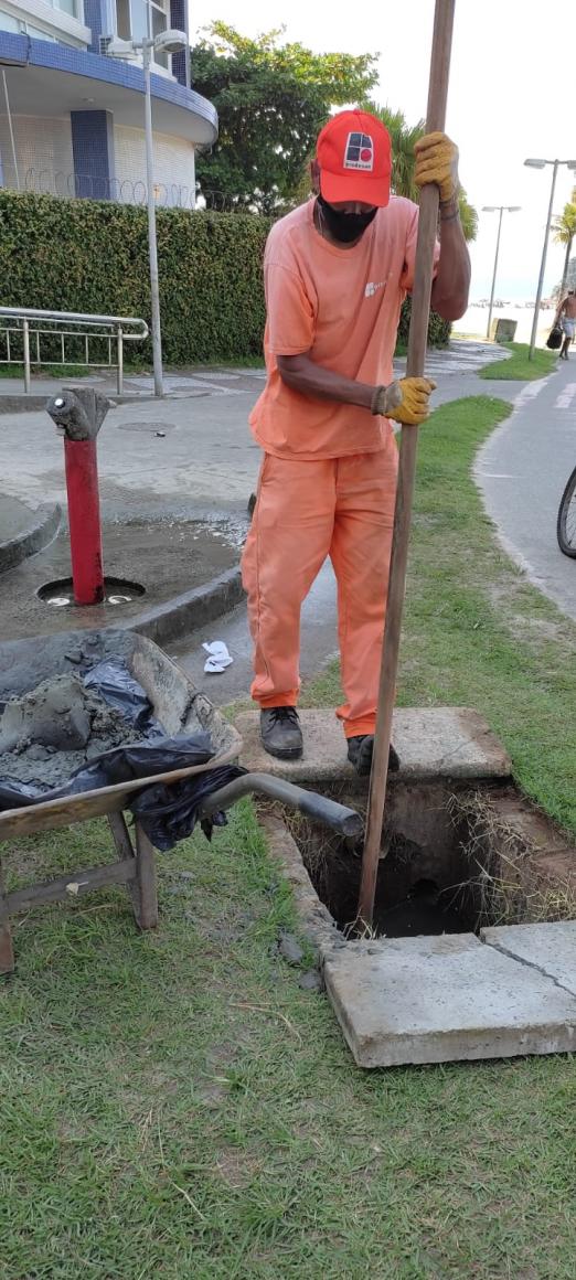 homem limpa caixa de drenagem ao lado de chuveirinho. #paratodosverem