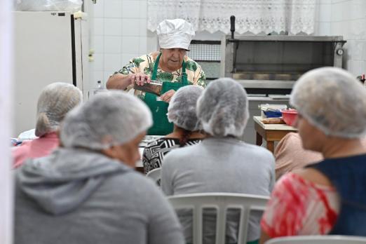 professora prepara doce enquanto é observada por alunas #paratodosverem 
