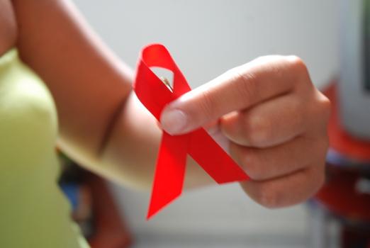 Mão de mulher segura laço vermelho que simboliza a luta contra a aids