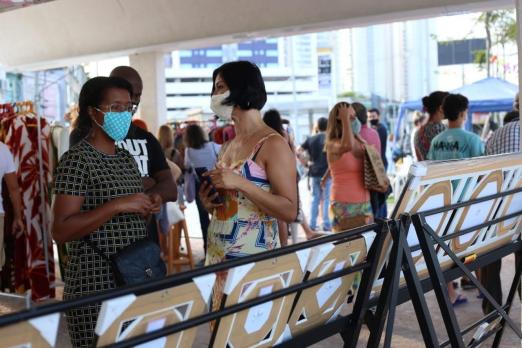 estande de quadros de costas para a foto, com pessoas circulando e conversando. Elas usam máscaras. #paratodosverem