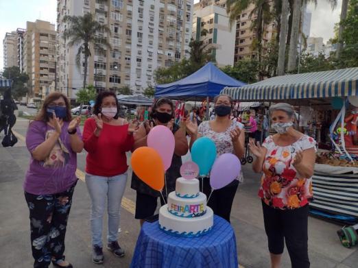pessoas comemoram com bolo em feira #paratodosverem