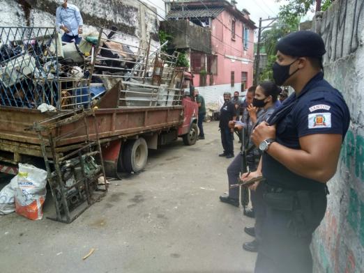 Guardas municipais à direita da foto observam caminhão carregado de objetos para ferro velho. #Paratodosverem