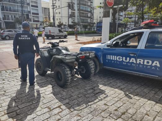 Guarda municipal está na orla ao lado de quadriciclo e viatura. #paratodosverem