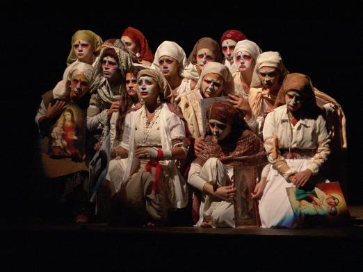 Foto de espetáculo. Vários artistas no palco, com roupas claras e turbantes. Estão todos reunidos. #Pracegover