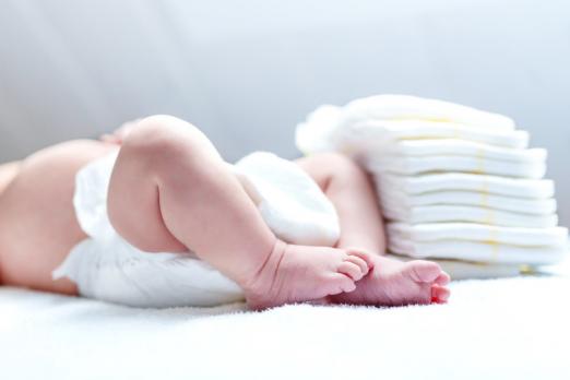 bebê está deitado usando fralda. Ao lado dele, uma pilha de fraldas descartáveis. #paratodosverem