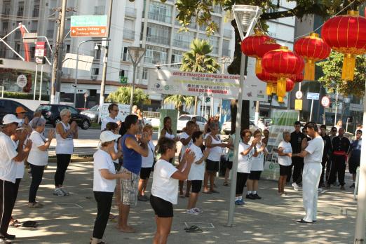 Praticantes fazem tai chi chuan em área ao ar livre. #Pracegover