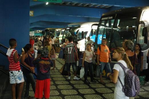 Pessoas transitando perto dos ônibus parados na rodoviária #pracegover 