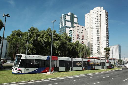 Vista geral do VLT sobre trilho em avenida. #Paratodosverem