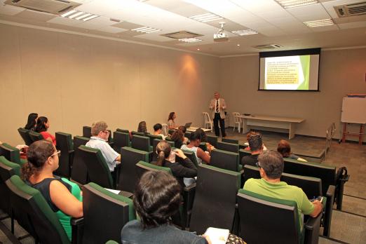 Auditório com servidores sentados assistindo palestra. Ao fundo aparece na parede uma imagem projetada. #Pracegover