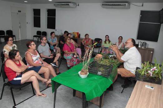 professor fala às alunas com orquideas na mesa #paratodosverem  