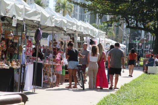 barracas de produtos artesanais em praça e pessoas circulando. #paratodosverem