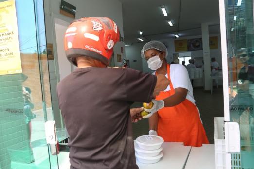 mulher entrega refeição a homem de capacete #paratodosverem 