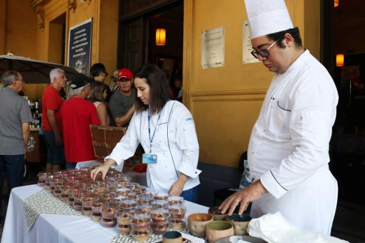 homem e mulher com roupas de chefs mexem em alimentos expostos #pracegover 