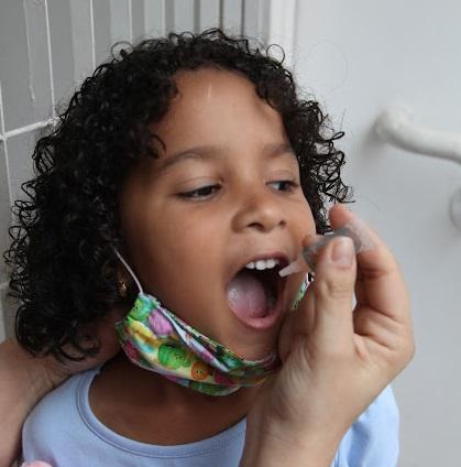 mão está pingando gota da vacina sabin na boca de uma menina. #paratodosverem