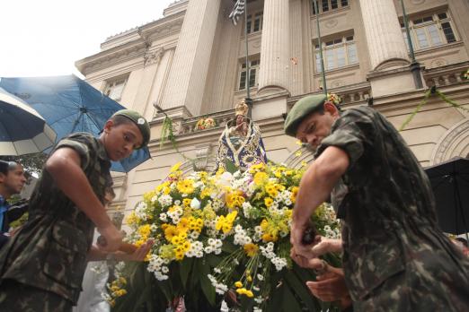 Imagem da Padroeira é carregada por dois soldados em frente à Prefeitura. A imagem está cercada de flores. #Pracegover