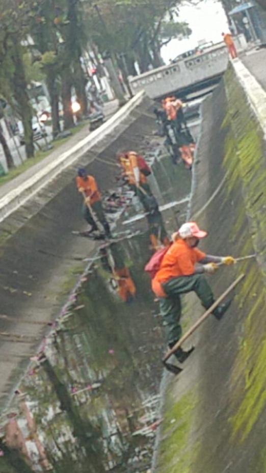 Funcionários da limpeza removem mato de paredes internas do canal. #pracegover