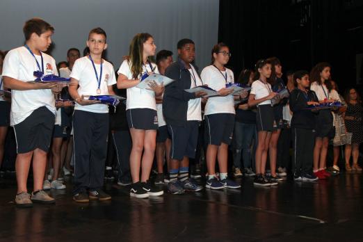 alunos premiados com medalhas e diplomas no palco #pracegover 