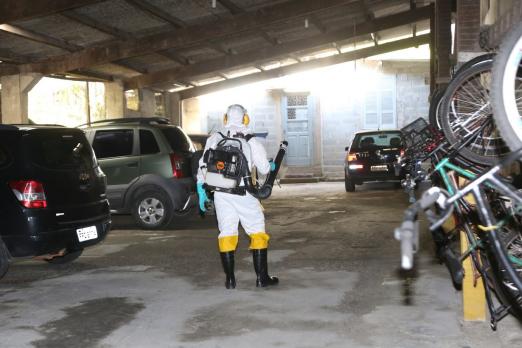 Homem paramentado aplica inseticida em garagem de veículos. #Paratodosverem