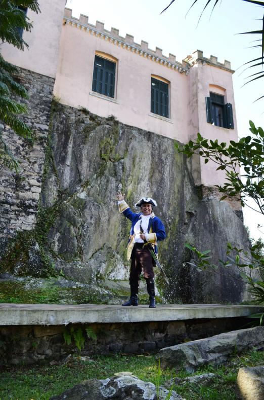 pirata posa para fonte em frente ao outeiro sobre o qual está incrustada uma casa. #paratodosverem