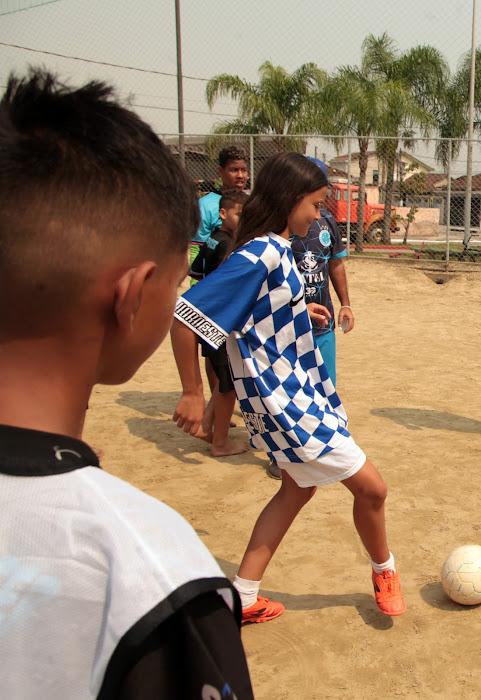 Menina chuta bola em campo de areia. #paratodosverem