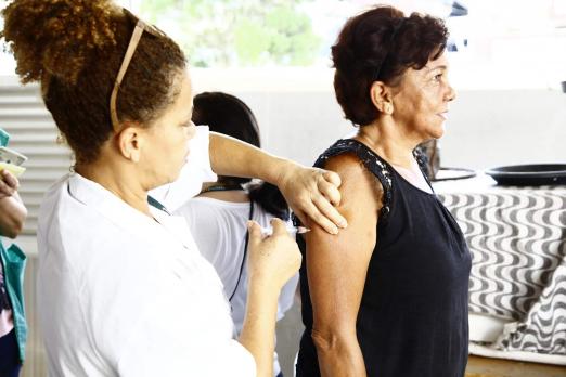 Mulher usando avental branco vacina uma outra mulher. #Pracegover