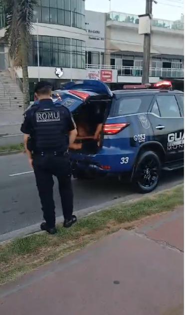 guarda municipal está ao lado de viatura com porta do bagageiro aberta. #paratodosverem 