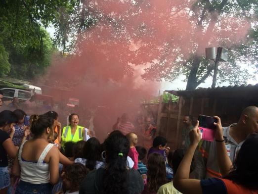 pessoas participam de simulado e olham fumaça vermelha subindo no exercicio #pracegover