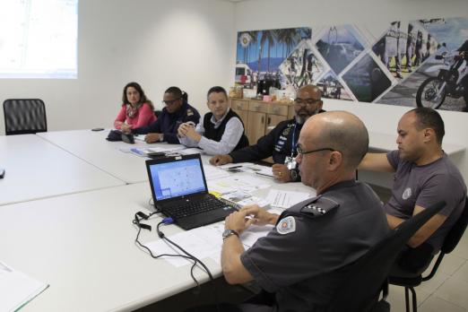 Pessoas reunidas em torno de uma mesa, com um quadro ao fundo. #Pracegover