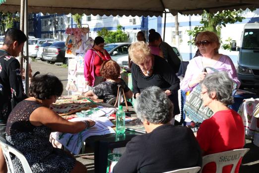 senhoras estão em mesa com bordados #pracegover 