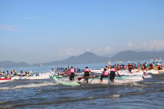 Canoas havaianas entram no mar. Atletas empurram as embarcações. #Pracegover