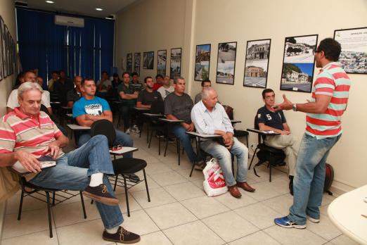 Alunos sentados em sala olham professor durante explicação #pracegover 