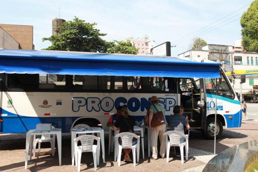 unidade móvel parada com pessoas sentadas em cadeiras na lateral #pracegover 