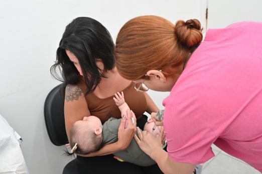 Mãe segura bebê para vacinação. #Paratodosverem