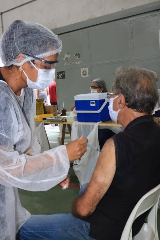 Mulher vacina homem que está sentado. #paratodosverem