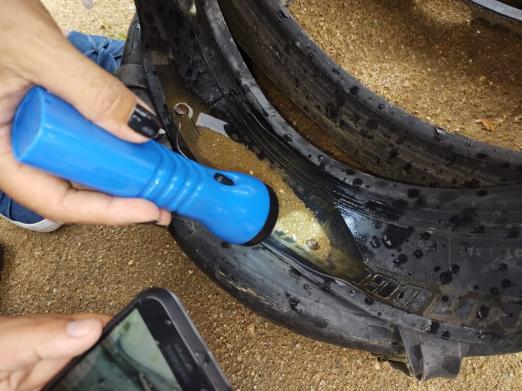 Imagem em close. Mão de mulher segura lanterna que ilumina parte interna de pneu de carro cheio de areia. #Paratodosverem