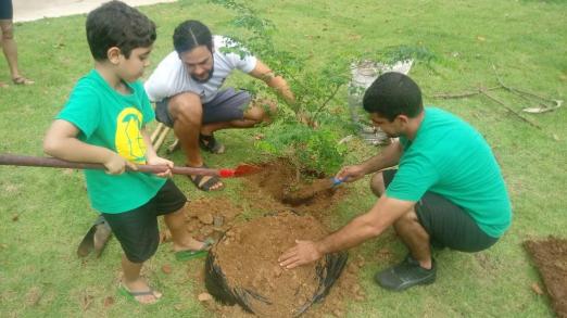 dois rapazes e criança plantam árvore #pracegover 