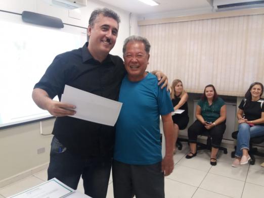 Professor e aluno se abraçam. Um deles segura um certificado em papel. #Pracegover