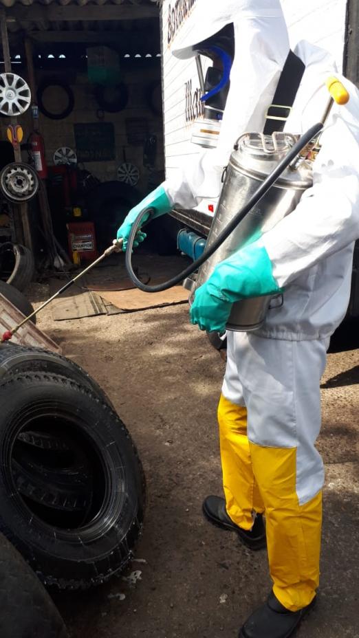 Homem uniformizado aplica inseticida com um jato em um pneu. #paratodosverem