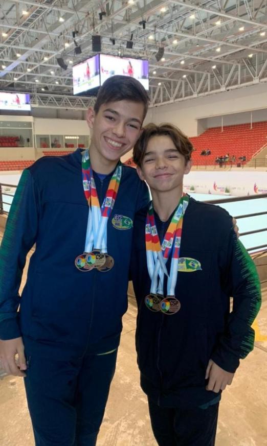 irmãos abraçados com medalhas em ginásio #paratodosverem