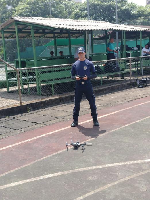 guarda municipal uniformizado segura controle remoto com drone voando à sua frente. #paratodosverem 