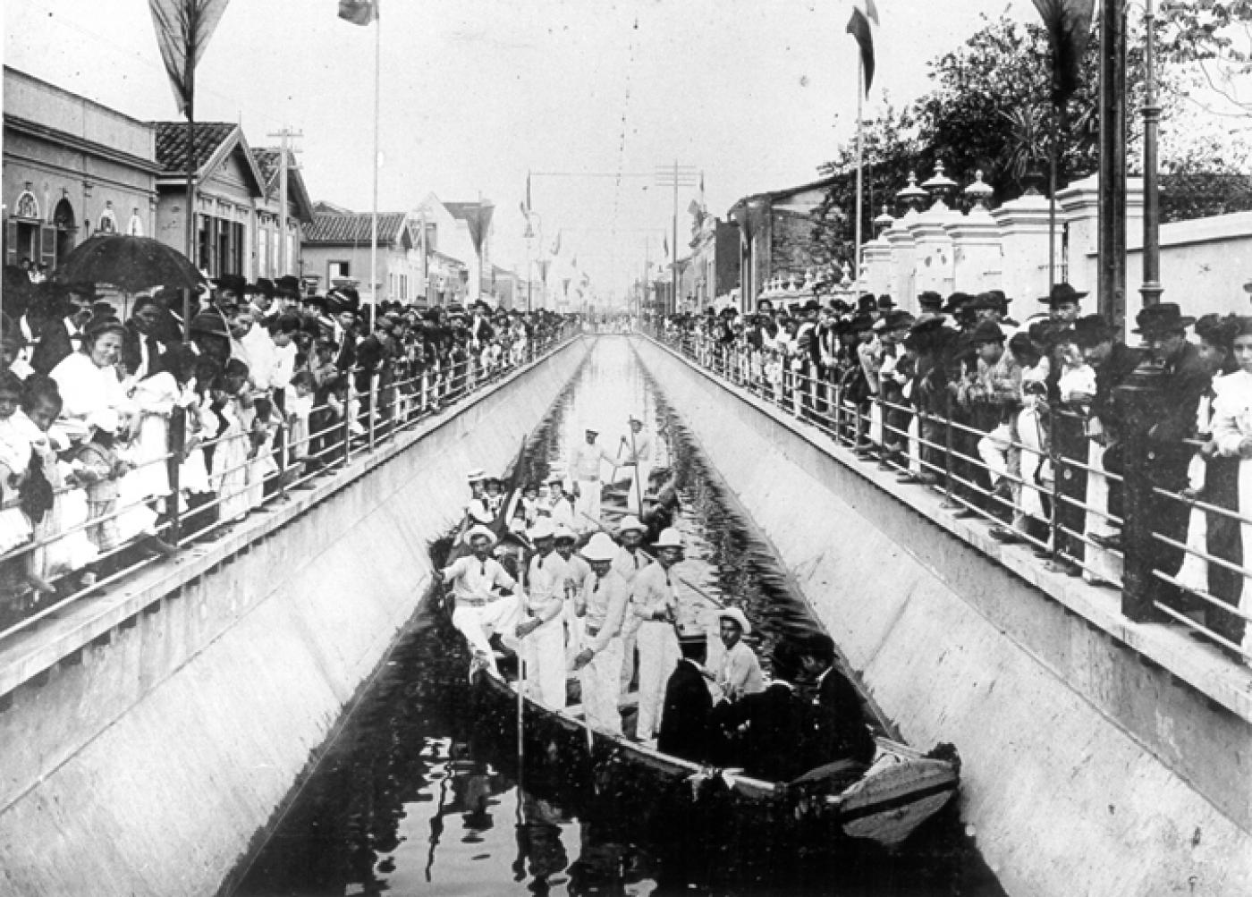 imagem de 1907 de inauguração de canal, com pessoas em embarcações dentro do canal, e fora, assistindo. #paratodosverem 