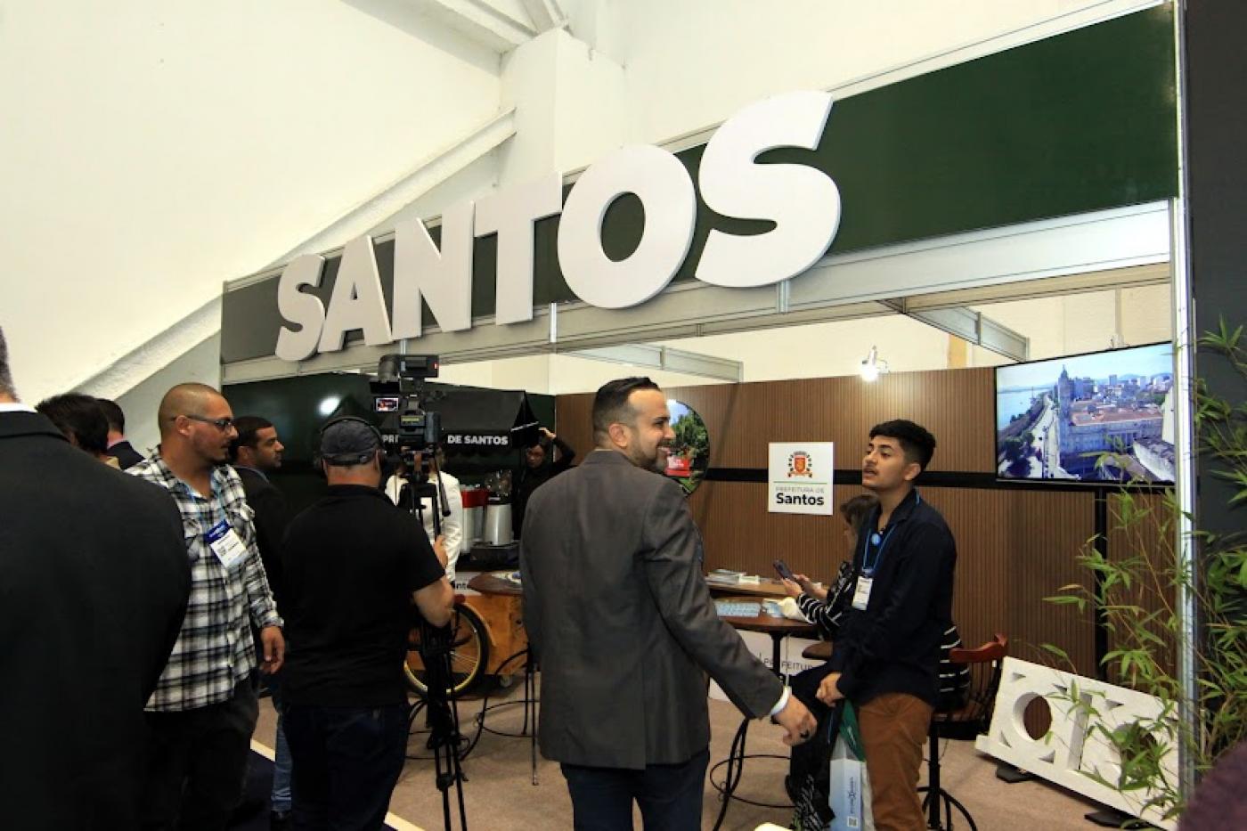 Estande com o letreiro escrito Santos em destaque é visitado por gestores e investidores. #pratodosverem