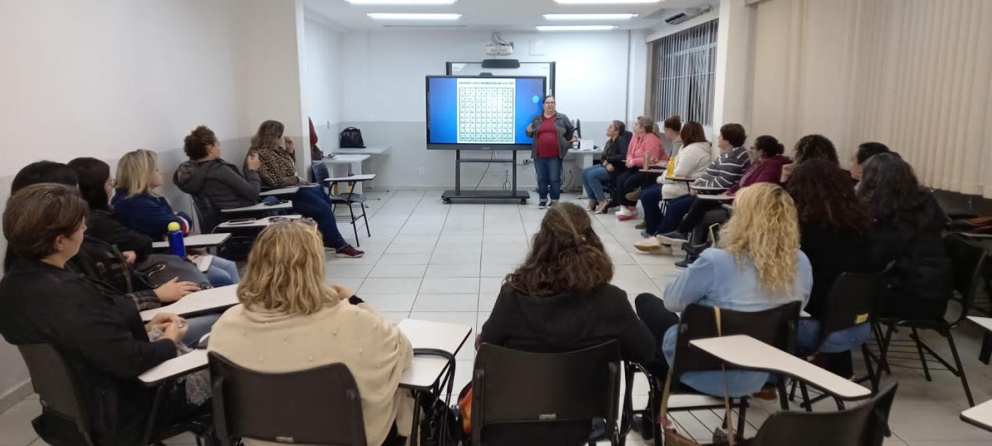 pessoas reunidas em sala de aula sentadas em cadeiras dispostas em formato de roda. Há um telão no fundo. #paratodosverem