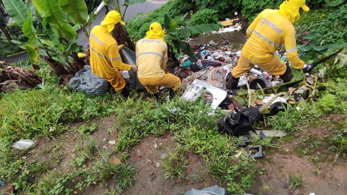 homens uniformizados estão agachados na encosta recolhendo lixo. #paratodosverem