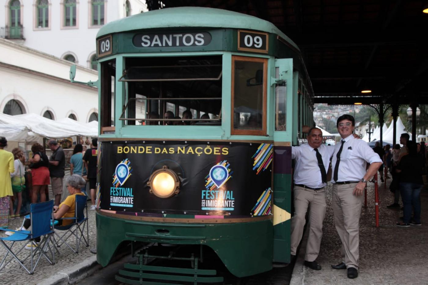 bonde das nações está parado na estação. várias pessoas estão em volta. #paratodosverem