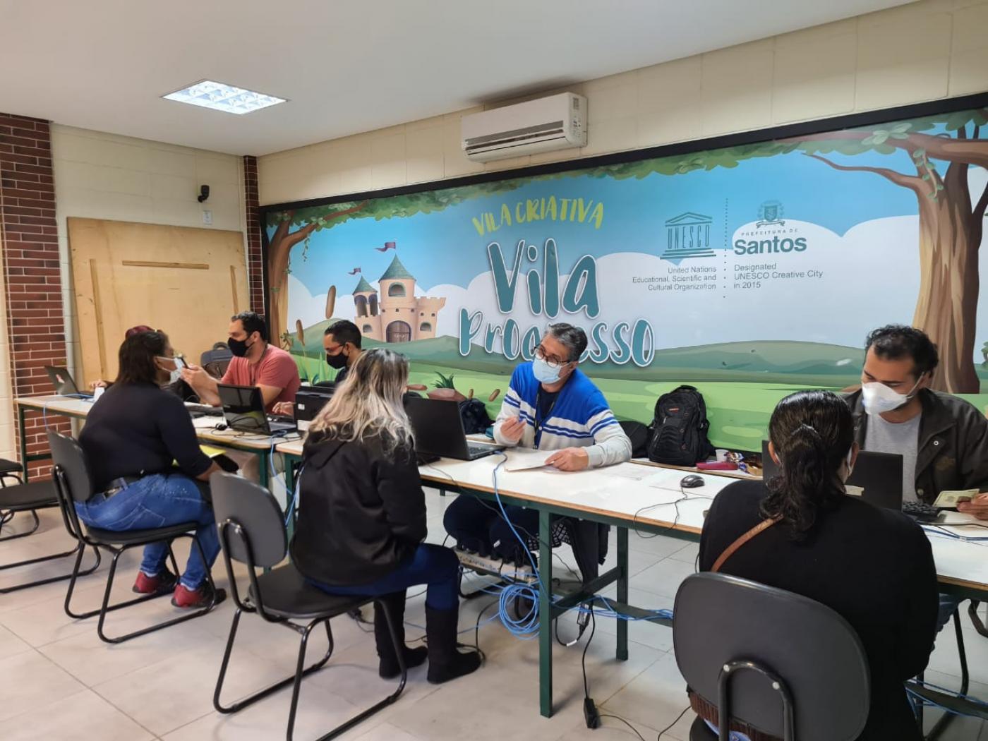 Pessoas sentadas sendo atendidas por funcionários. #paratodosverem