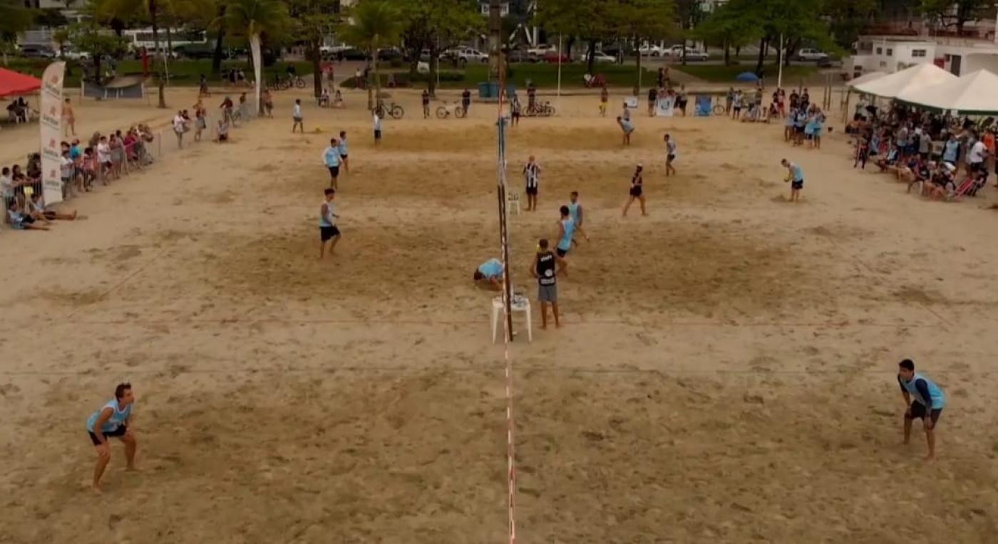 Várias pessoas em competição de futevolei na areia da praia #paratodosverem