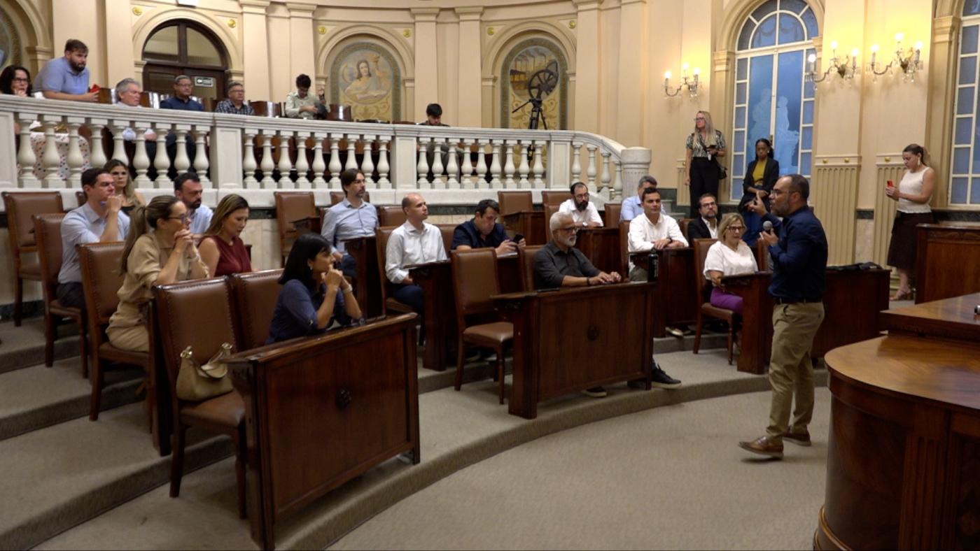 sala princesa isabel com secretários sentados e um deles em pé falando ao grupo. #paratodosverem 