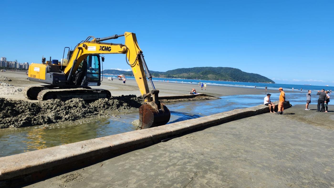 escavadeira está na beira do canal na praia recolhendo areia acumulada. #paratodosverem