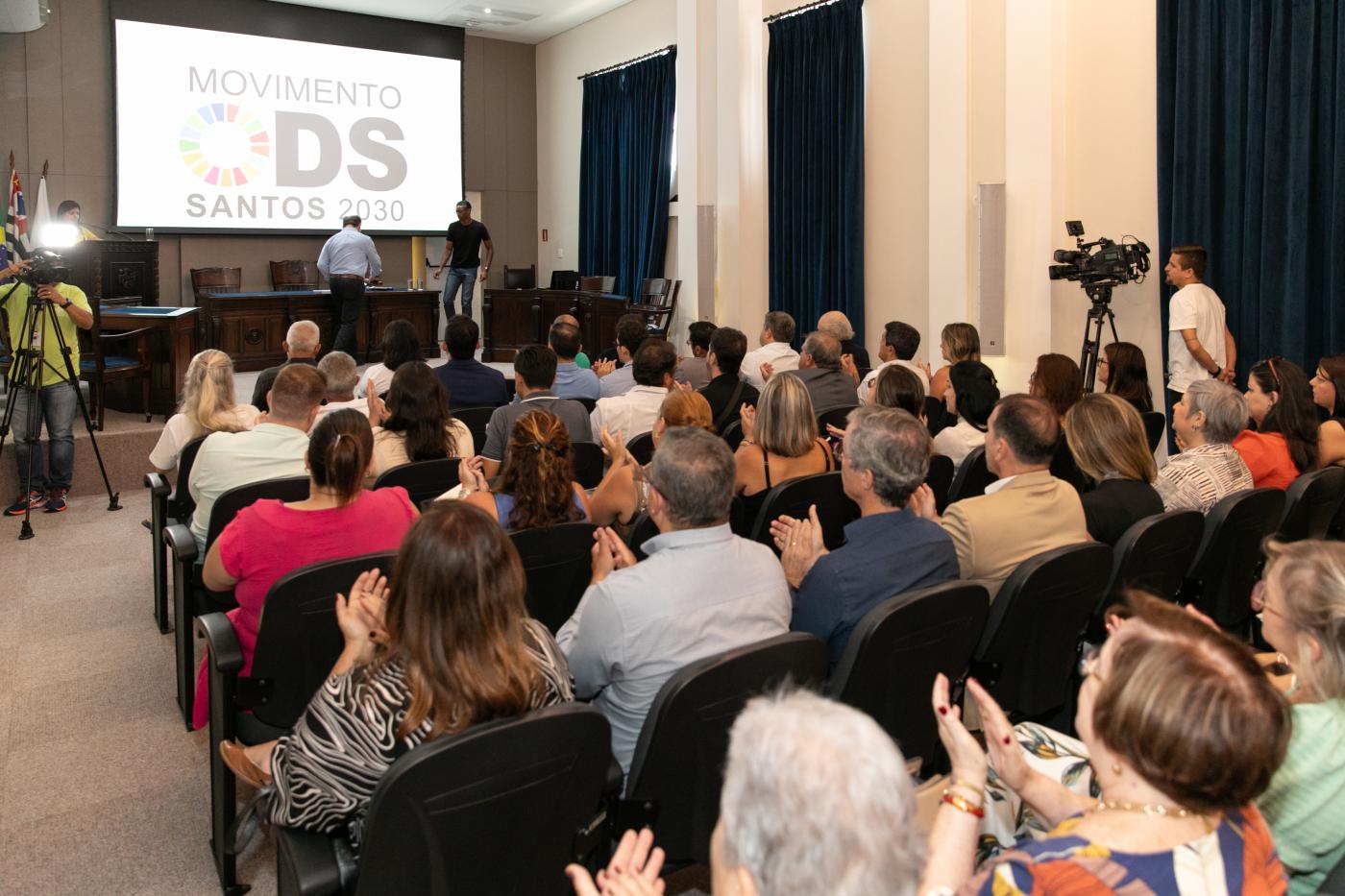 auditório lotado de pessoas assistindo apresentação. #paratodosverem 